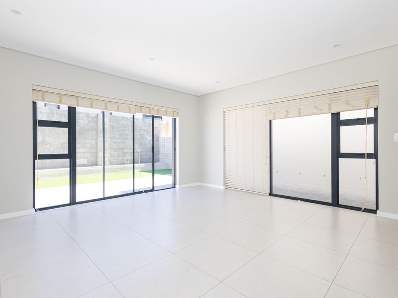 A bright, spacious, and empty living area featuring large format floor tiles, recessed downlights, and expansive aluminium sliding doors leading to the outdoor space.