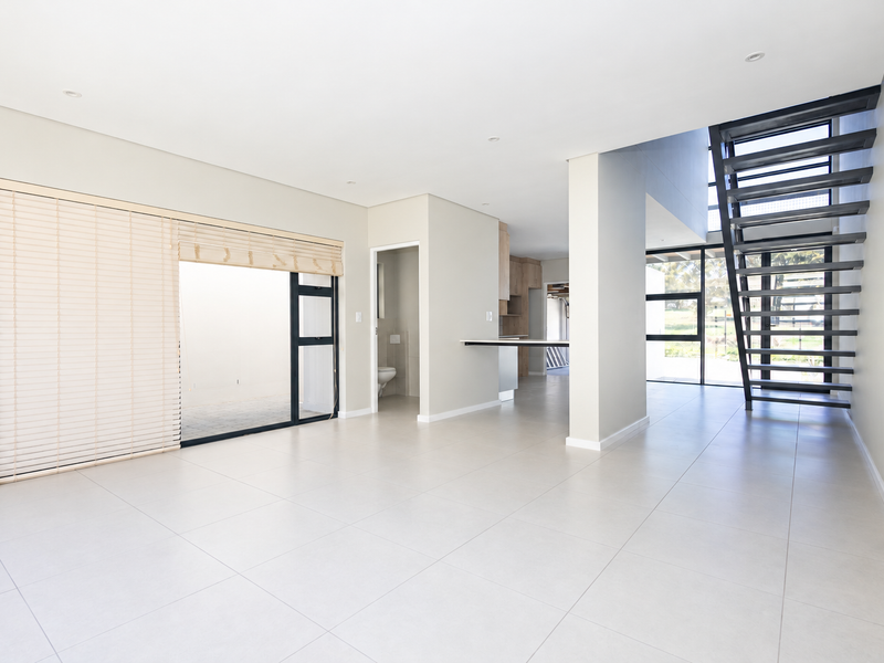 Spacious open-plan living area featuring modern tiled floors, a striking metal staircase, and large sliding glass doors leading to an outdoor space.