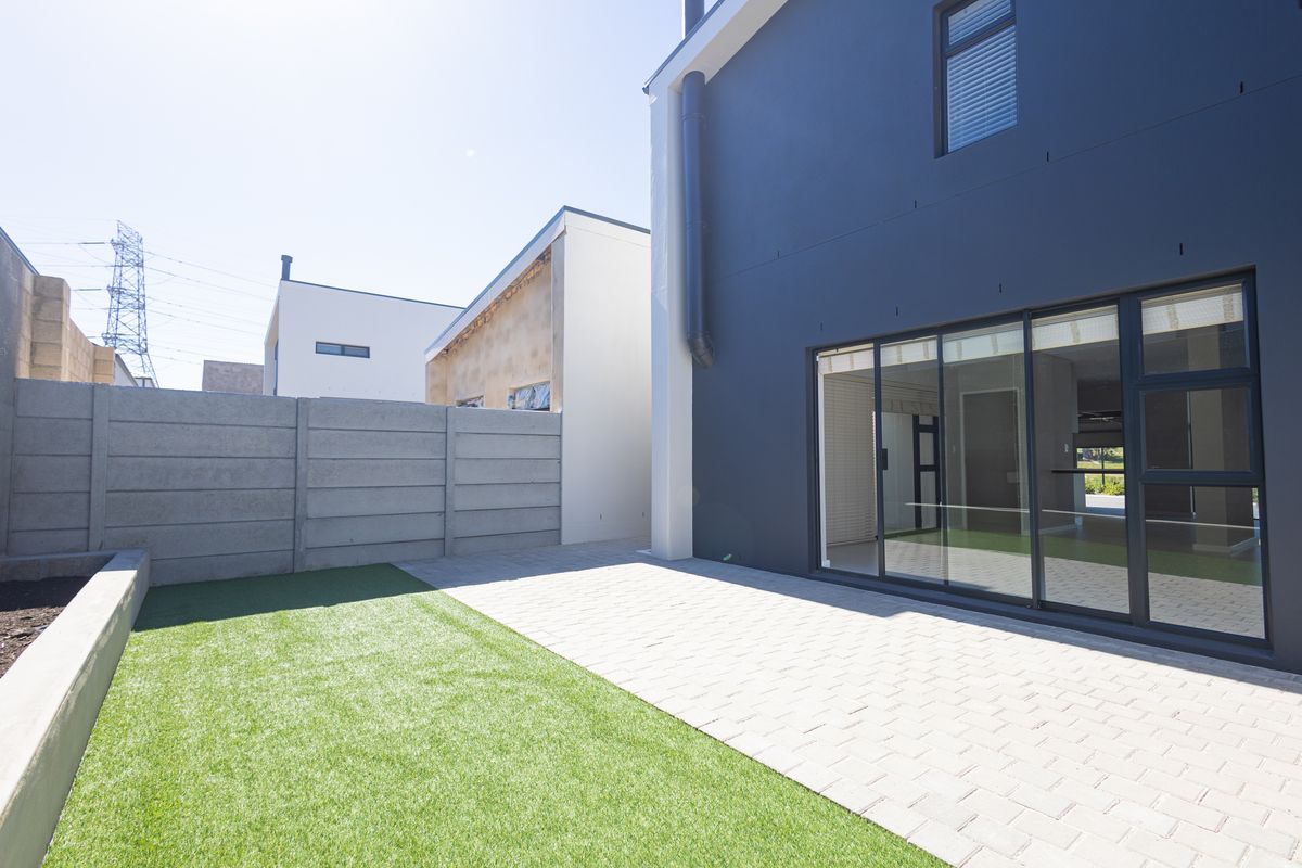 Rear view of the townhouse featuring a paved patio area, artificial lawn, and modern dark-toned exterior facade with large sliding glass doors.