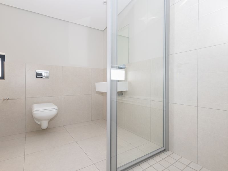 Modern bathroom featuring a wall-mounted toilet, wall-mounted basin, and a glass-enclosed shower with neutral floor-to-ceiling tiling.