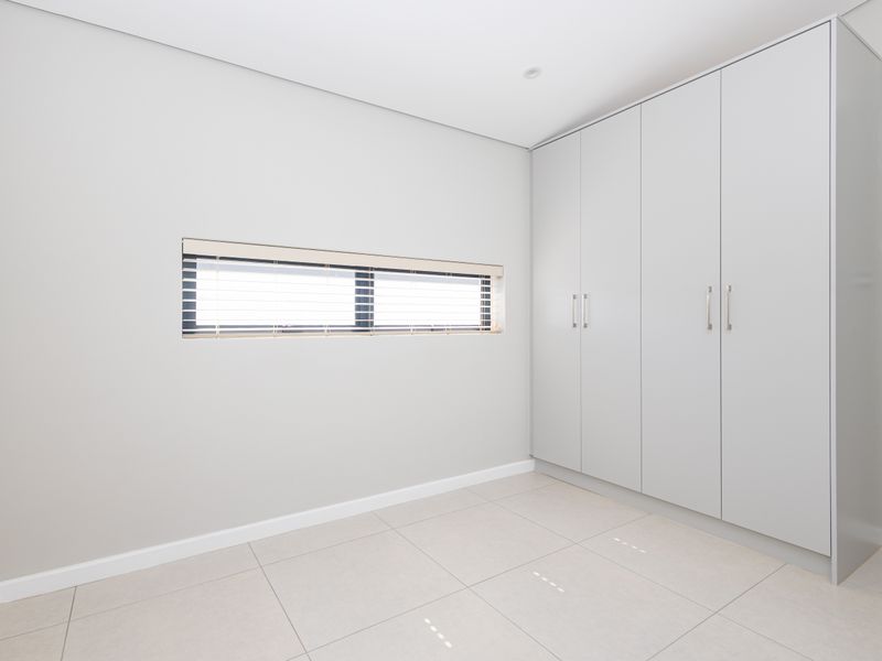 A clean, modern bedroom featuring neutral grey walls, large format floor tiles, and a spacious built-in wardrobe with sleek hardware.