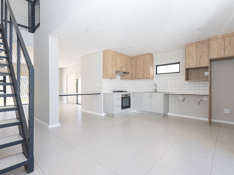 Modern open-plan kitchen featuring light wood cabinetry, built-in appliances, and a sleek staircase, set against a neutral tiled floor in a bright, spacious layout.