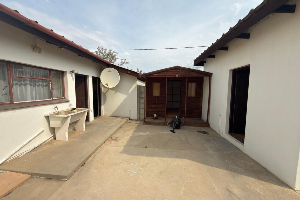 Rear courtyard area featuring a concrete patio, external utility sink, and a detached timber outbuilding structure.