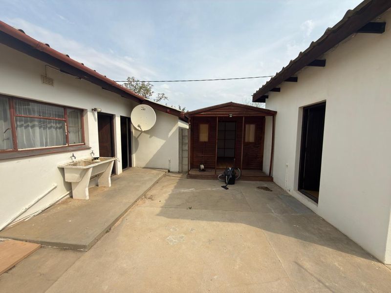 Rear courtyard area featuring a concrete patio, external utility sink, and a detached timber outbuilding structure.
