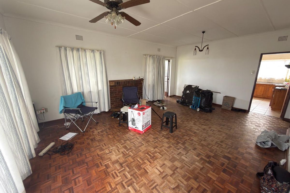 Spacious living room featuring classic parquet flooring, a brick fireplace, and a ceiling fan, offering a blank canvas for interior design.
