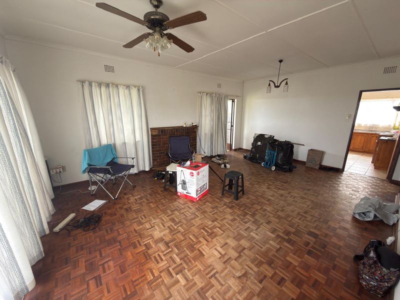 Spacious living room featuring classic parquet flooring, a brick fireplace, and a ceiling fan, offering a blank canvas for interior design.