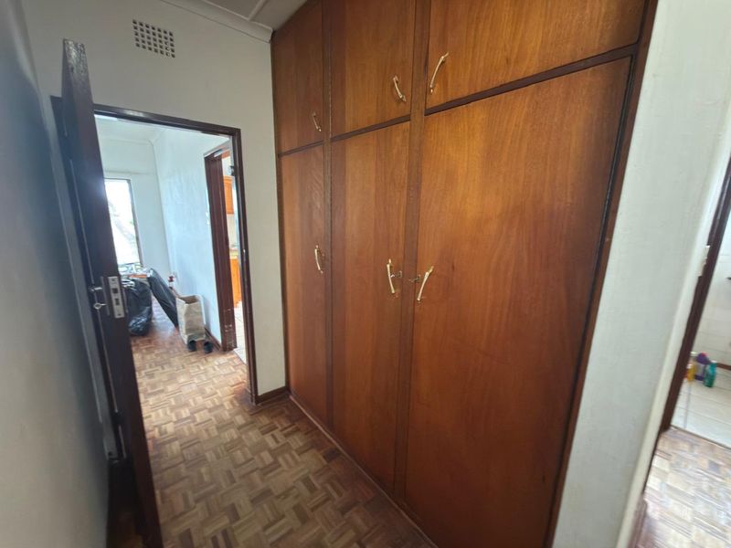 A hallway featuring classic parquet flooring and extensive built-in wooden cabinetry, providing ample storage space.