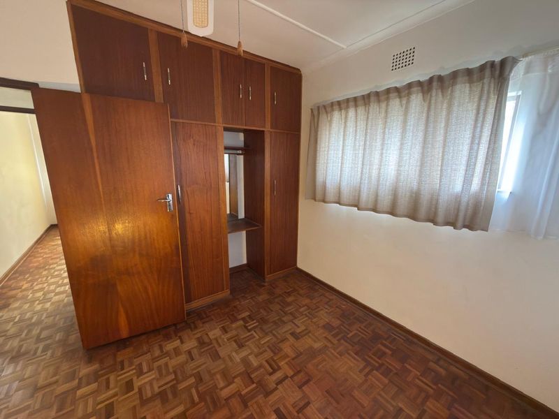 A bedroom featuring classic parquet flooring and extensive built-in wooden cabinetry, offering a functional space with a traditional aesthetic.