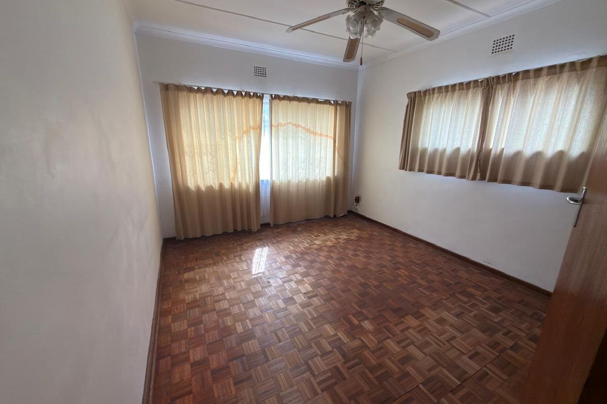 An empty bedroom featuring original parquet flooring, a ceiling fan, and large windows with neutral curtains.