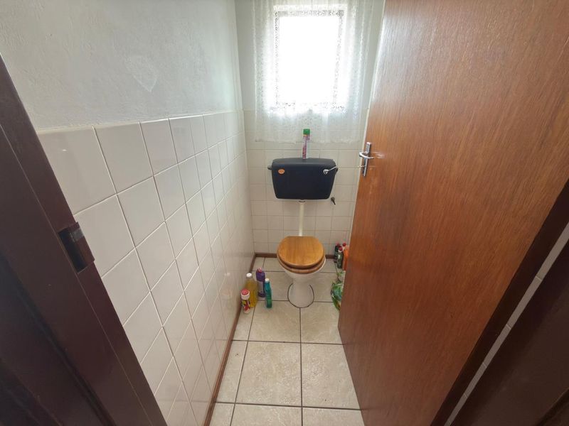 A small, functional guest bathroom featuring a toilet, tiled walls, and tiled flooring, currently in a dated condition.
