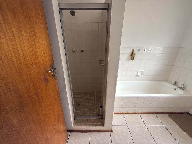A functional bathroom featuring a separate shower enclosure, a built-in bathtub, and neutral wall and floor tiling throughout.