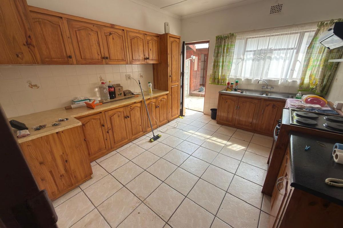 A functional kitchen featuring traditional wooden cabinetry, laminate countertops, a double basin sink, and ceramic floor tiles with direct access to the rear exterior.