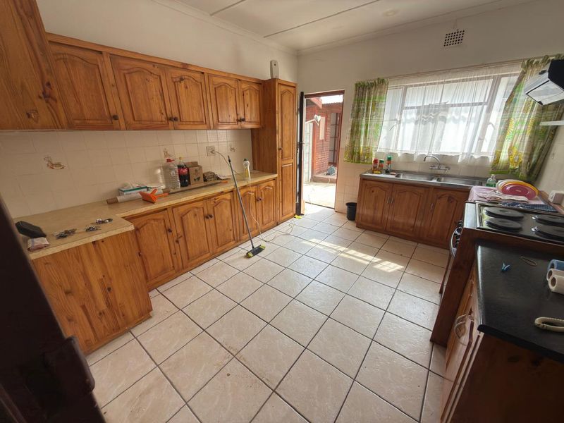 A functional kitchen featuring traditional wooden cabinetry, laminate countertops, a double basin sink, and ceramic floor tiles with direct access to the rear exterior.