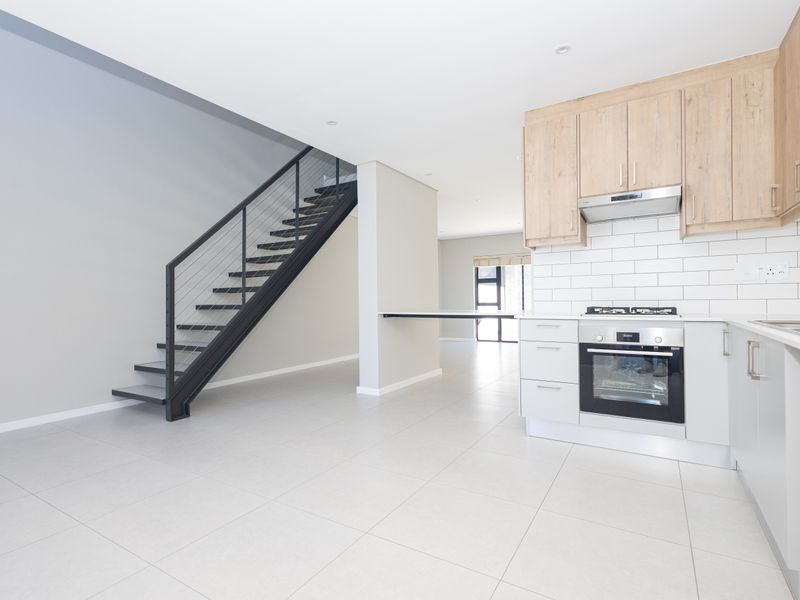 Modern open-plan kitchen and living area featuring sleek cabinetry, integrated appliances, subway tile backsplash, and a contemporary metal staircase.
