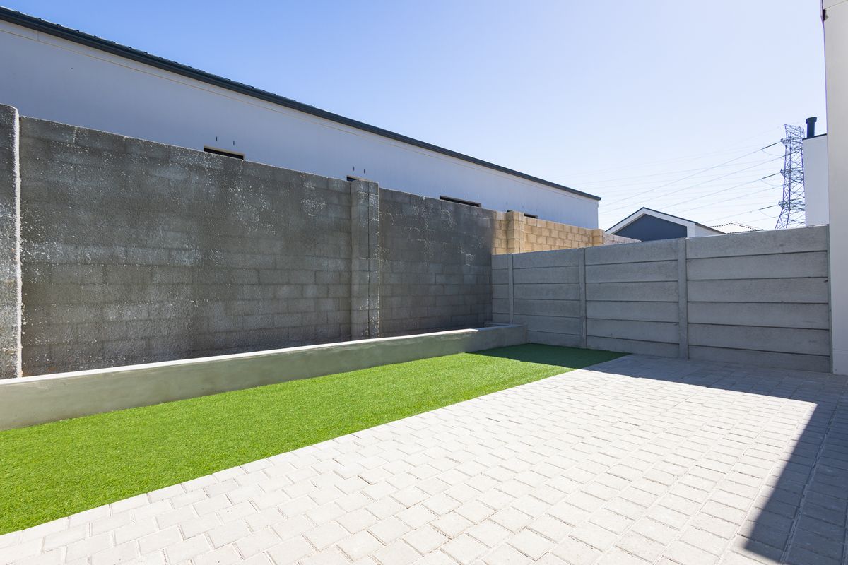 A private rear courtyard featuring a paved patio area, artificial lawn, and high concrete boundary walls.