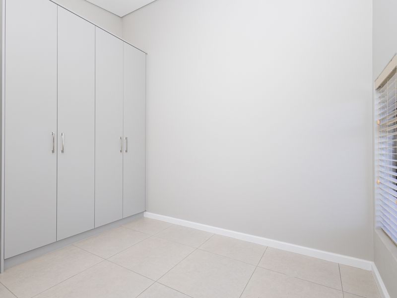 A clean, empty bedroom featuring neutral tiled flooring, light grey walls, and a large built-in wardrobe with modern hardware.