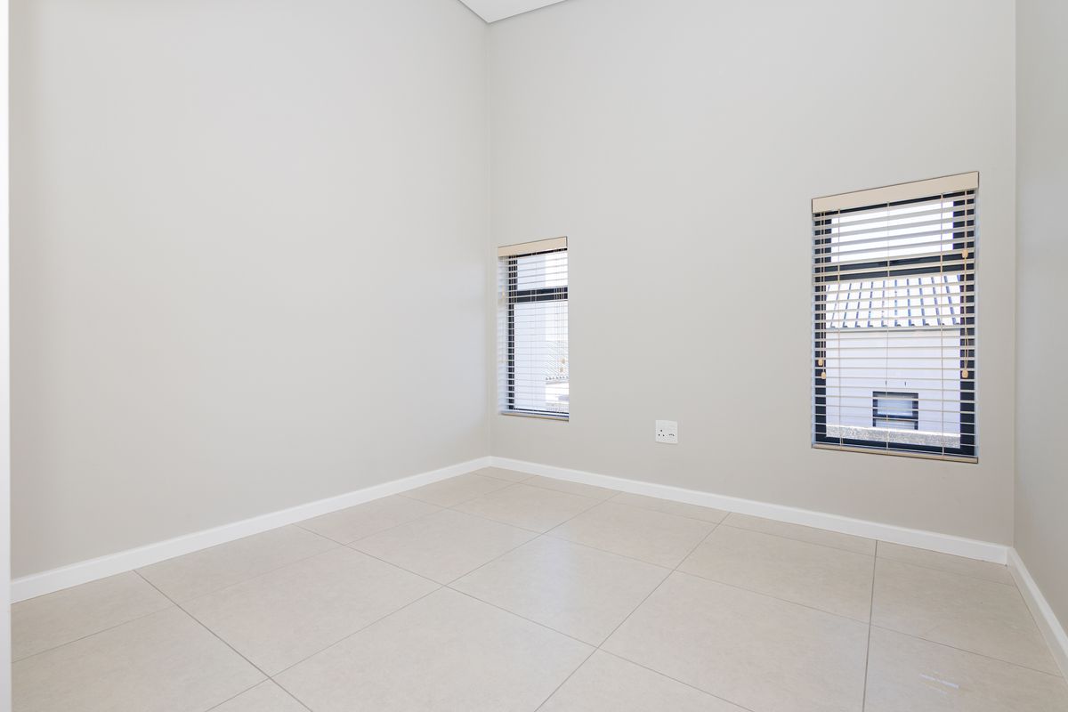 A bright, empty bedroom featuring neutral tiled flooring, clean walls, and modern aluminium windows with fitted venetian blinds.
