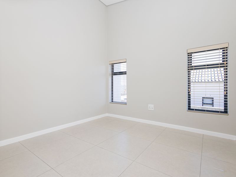 A bright, empty bedroom featuring neutral tiled flooring, clean walls, and modern aluminium windows with fitted venetian blinds.