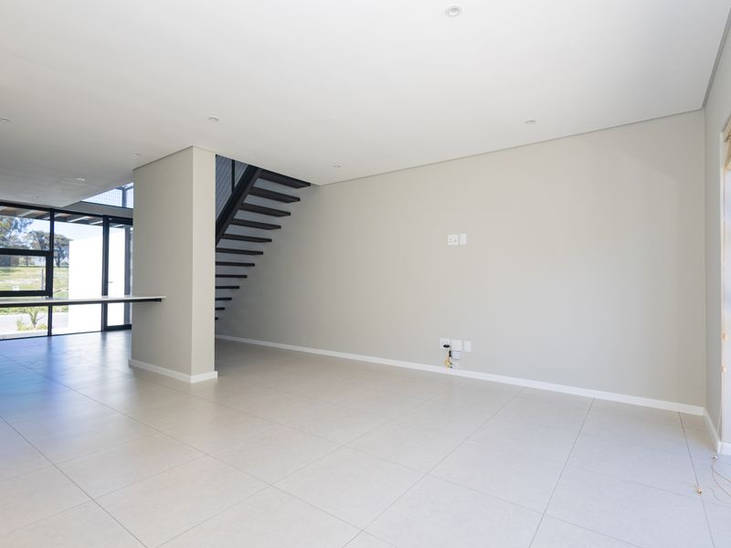 A bright, modern, and spacious open-plan living area featuring large glass doors, tiled floors, and a contemporary staircase.