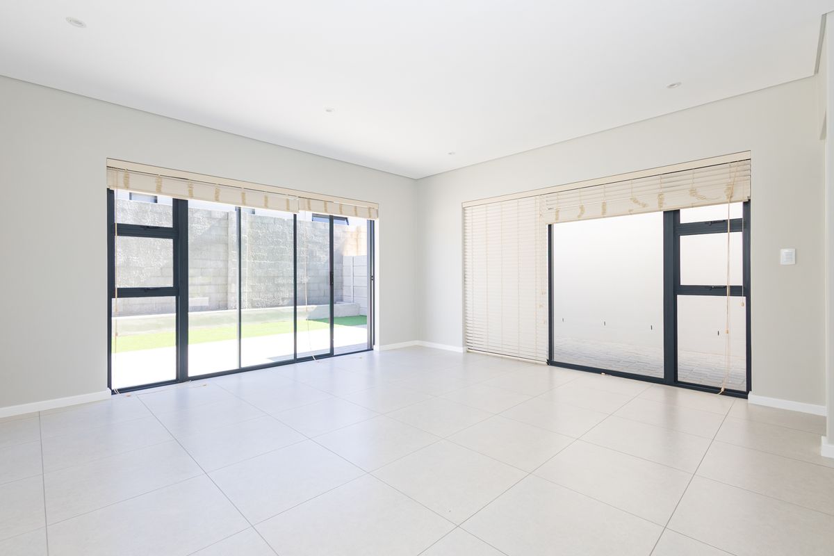 A bright, spacious, and empty living area featuring large aluminium sliding doors, neutral tiled flooring, and modern recessed downlights.