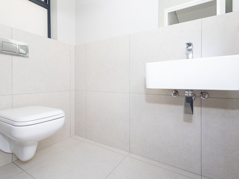 A modern, minimalist guest bathroom featuring a wall-mounted toilet with a concealed cistern and a sleek wall-mounted basin with chrome fixtures.