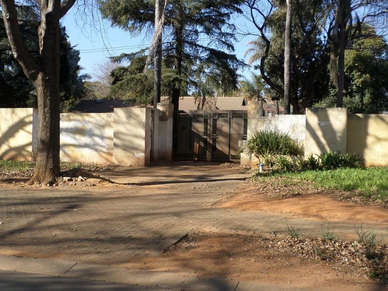 Front view of the property featuring a paved driveway, metal entrance gate, and a perimeter wall with visible weathering.