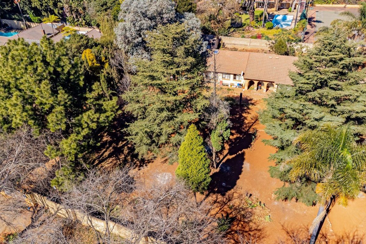 Aerial view of a residential property featuring a tiled roof house, an arched patio, and extensive mature garden landscaping.