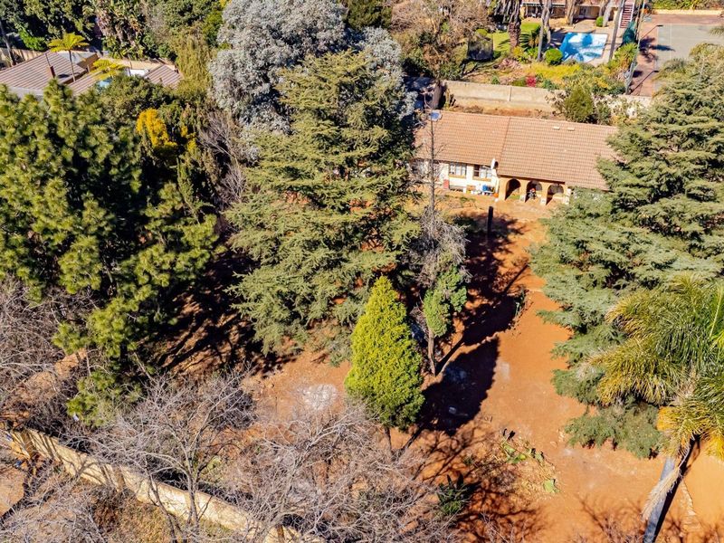 Aerial view of a residential property featuring a tiled roof house, an arched patio, and extensive mature garden landscaping.