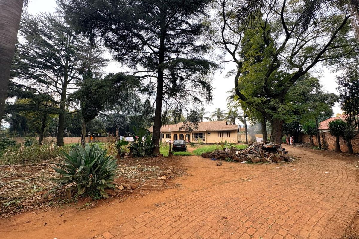 A wide-angle view of the property front elevation featuring a paved driveway, mature trees, and a large garden area.