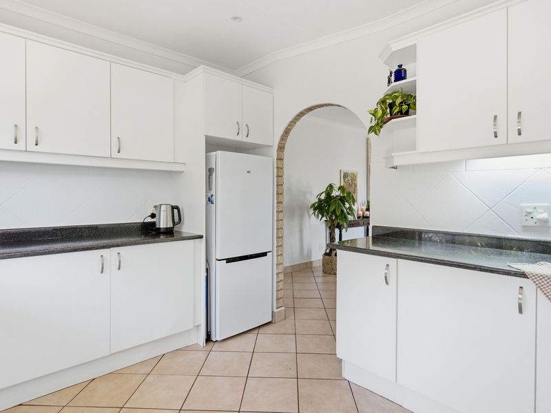 A clean, functional kitchen featuring white cabinetry, dark granite countertops, and a distinctive arched brick entryway leading to the adjacent living space.