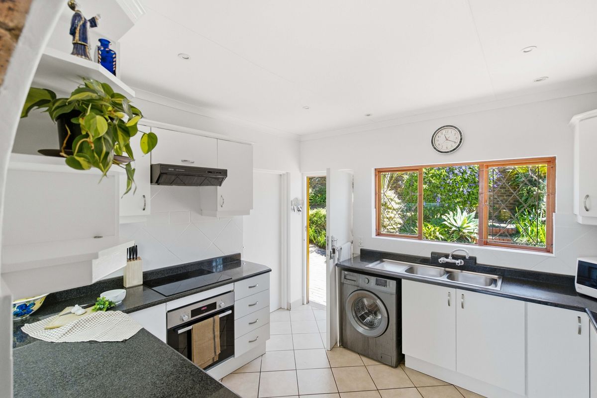A functional kitchen featuring white cabinetry, dark granite countertops, built-in oven and hob, and direct access to the garden.