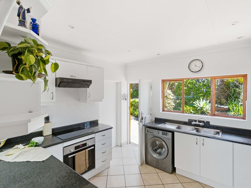 A functional kitchen featuring white cabinetry, dark granite countertops, built-in oven and hob, and direct access to the garden.