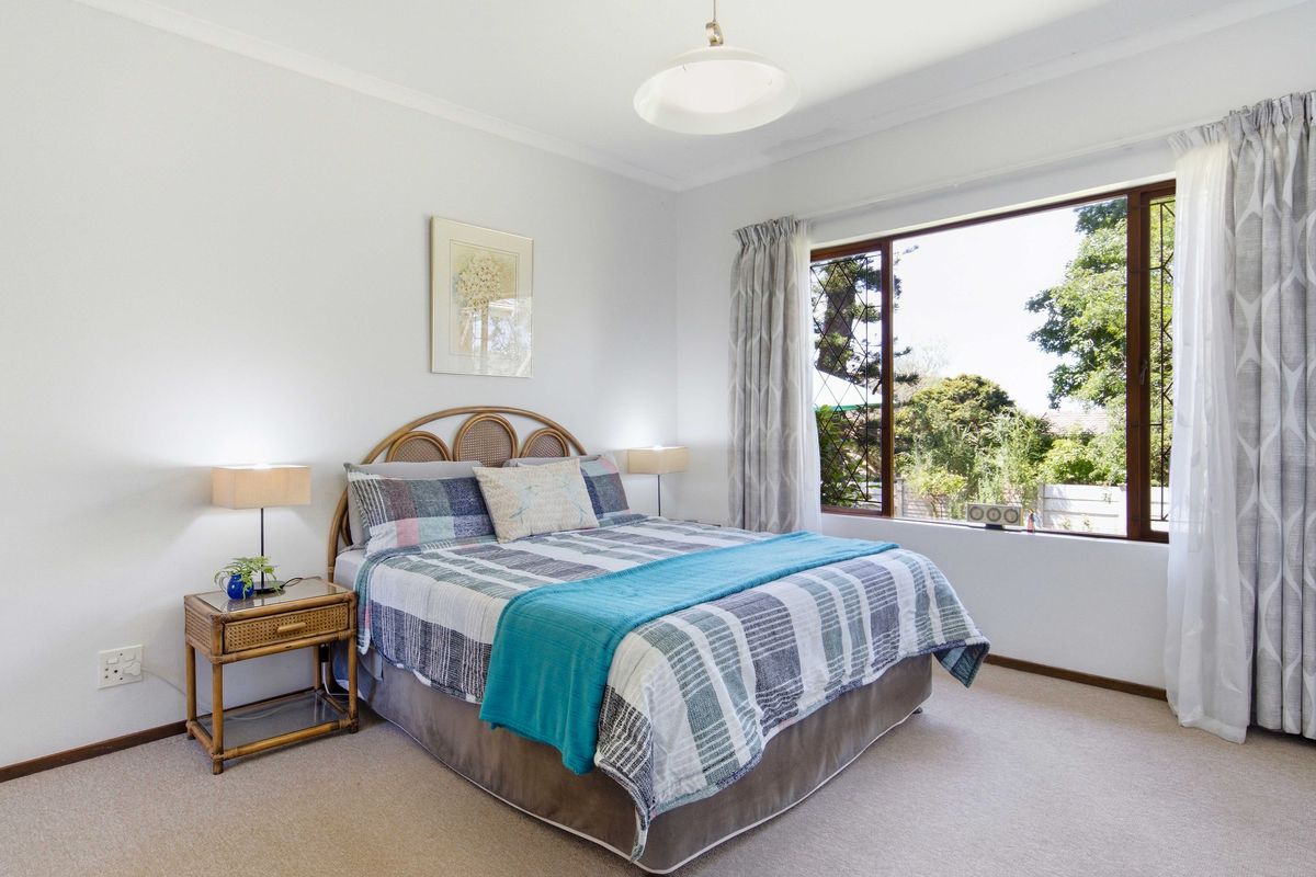 A bright and well-maintained bedroom featuring neutral walls, carpeted flooring, and a large window providing natural light and garden views.