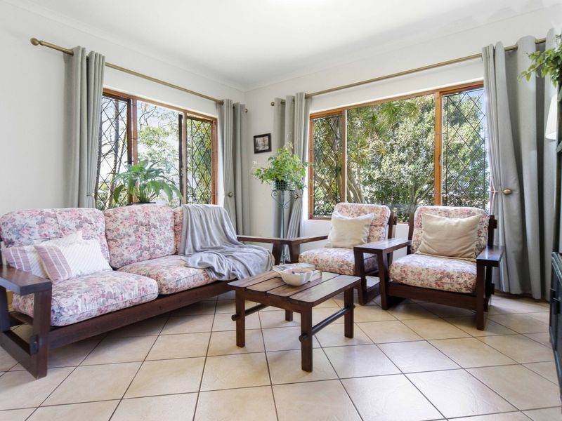 A bright living room featuring large leaded glass windows, neutral ceramic floor tiles, and coved cornicing, offering a pleasant view of the surrounding greenery.