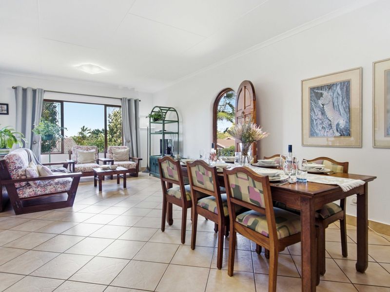 Spacious open-plan living and dining area featuring tiled flooring, natural light, and an arched wooden door leading to the exterior.