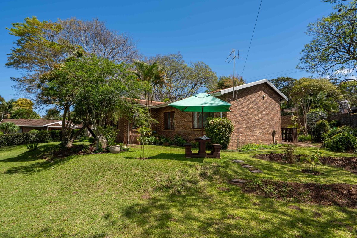 A view of the rear exterior of the townhouse, featuring a face brick facade, tiled roof, and a well-maintained garden area.