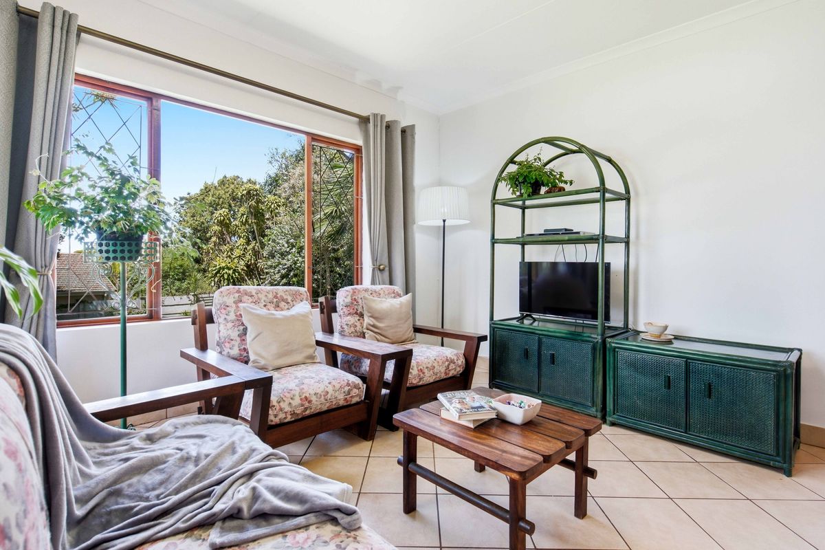 A bright living room featuring tiled flooring and a large window providing natural light and garden views.