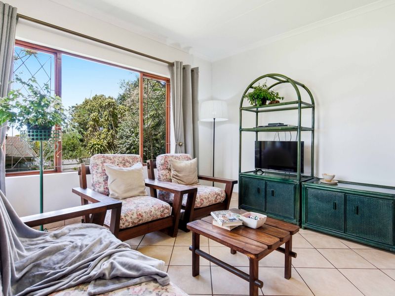 A bright living room featuring tiled flooring and a large window providing natural light and garden views.