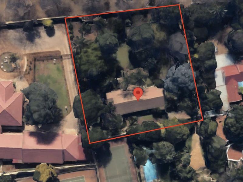 An aerial view of a residential plot featuring mature trees and a central structure, outlined with a red boundary marker.