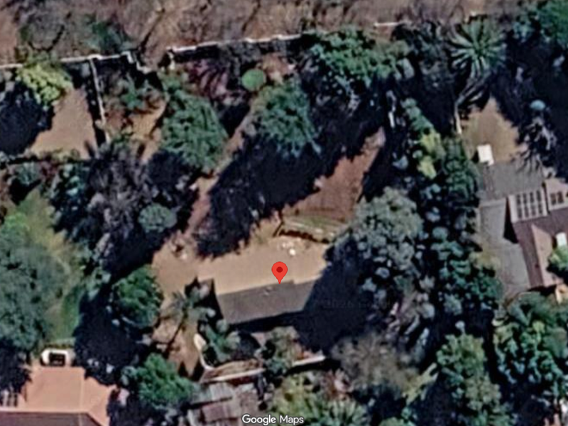 An aerial satellite view of a residential property plot featuring established trees and boundary walls.