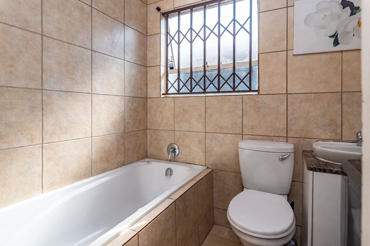 A functional bathroom featuring a bathtub, toilet, and vanity basin with tiled walls and a security-gated window.