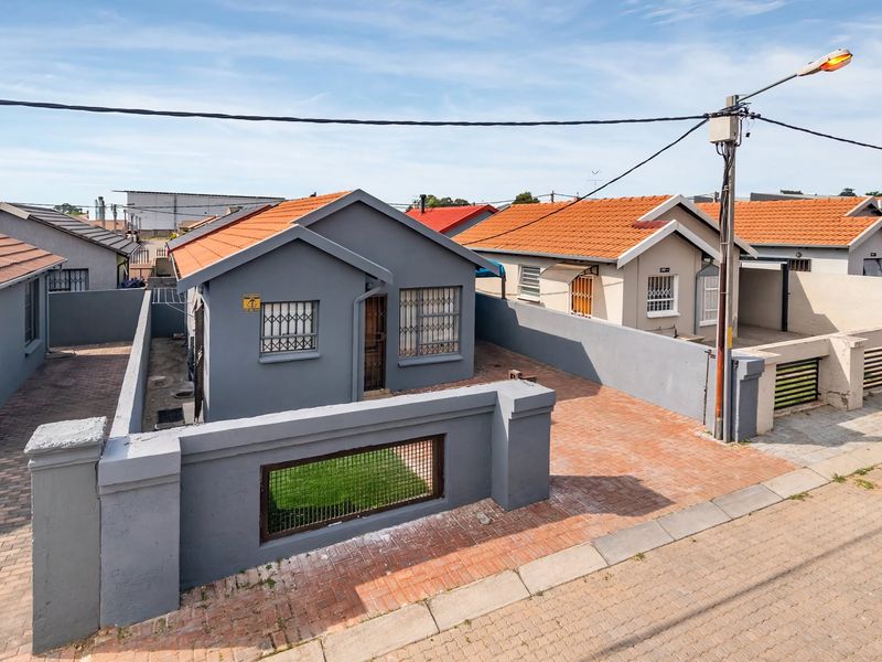 Front view of a detached residential house featuring a paved driveway, perimeter wall, and secure window bars.