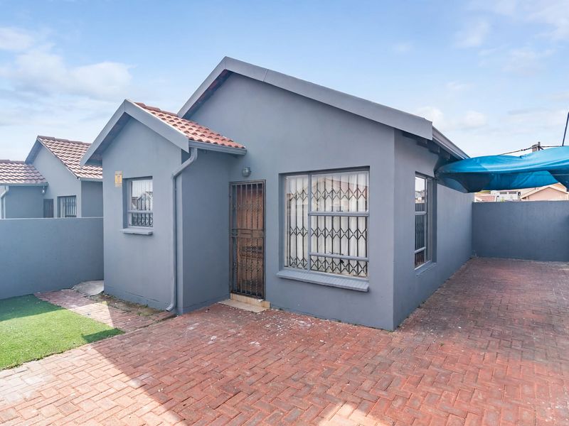 Front view of a detached house featuring a grey painted facade, tiled roof, paved driveway, and secure window and door fittings.