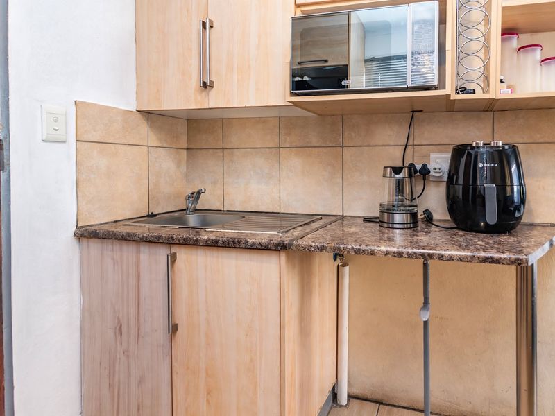 A compact scullery or kitchenette area featuring laminate cabinetry, a stainless steel sink, tiled backsplash, and a granite-look laminate countertop.