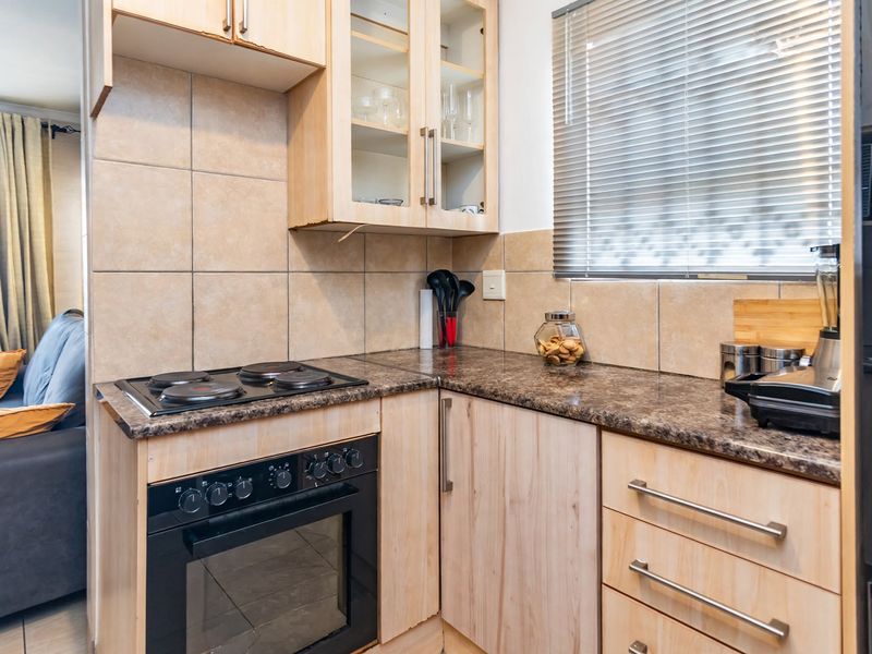 Compact kitchen featuring light wood cabinetry, granite countertops, tiled backsplash, and a built-in electric oven and hob.
