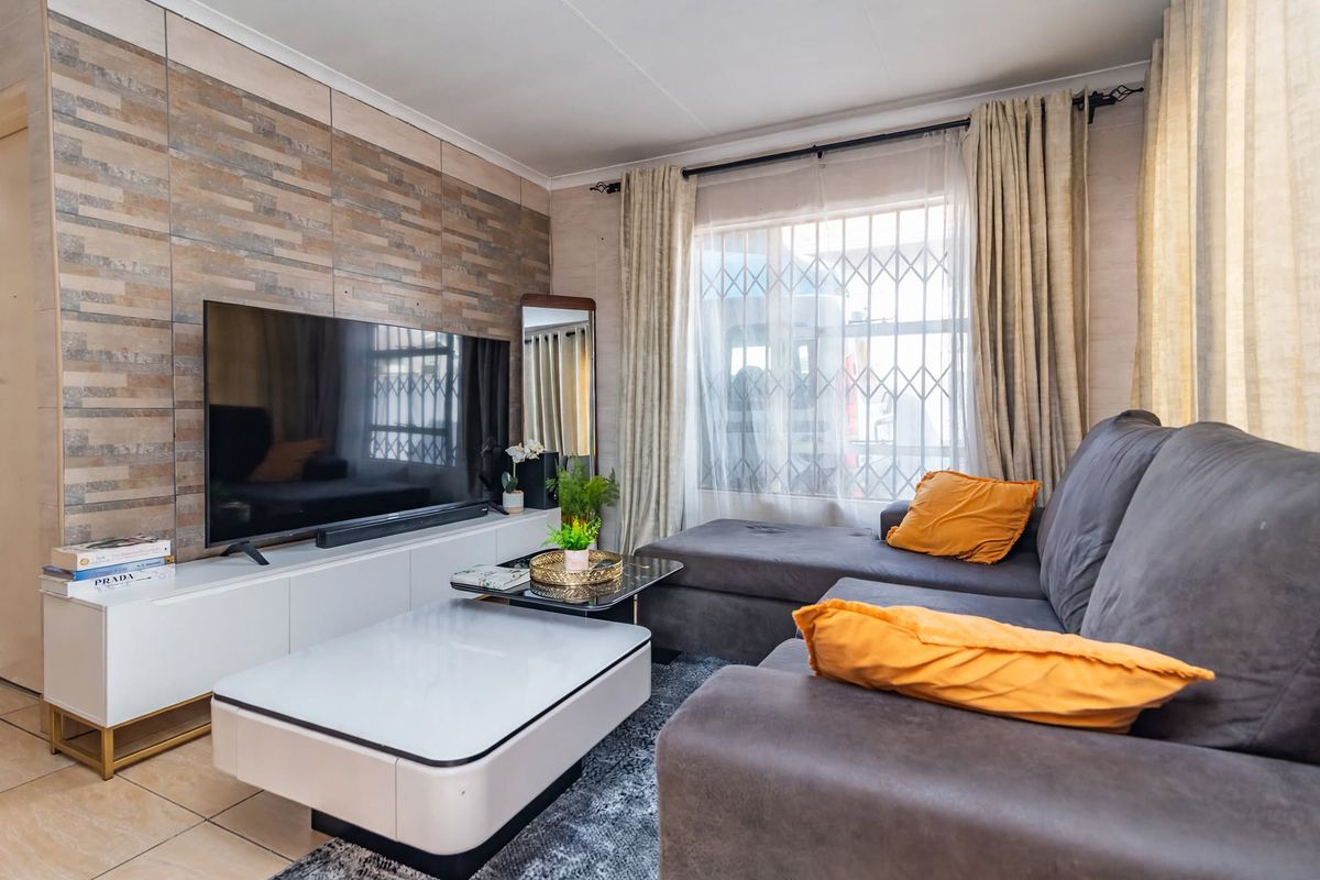 A comfortable living room featuring tiled flooring and a decorative textured feature wall, complete with a window fitted with a security gate.