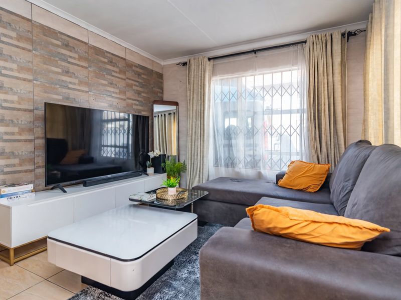 A comfortable living room featuring tiled flooring and a decorative textured feature wall, complete with a window fitted with a security gate.