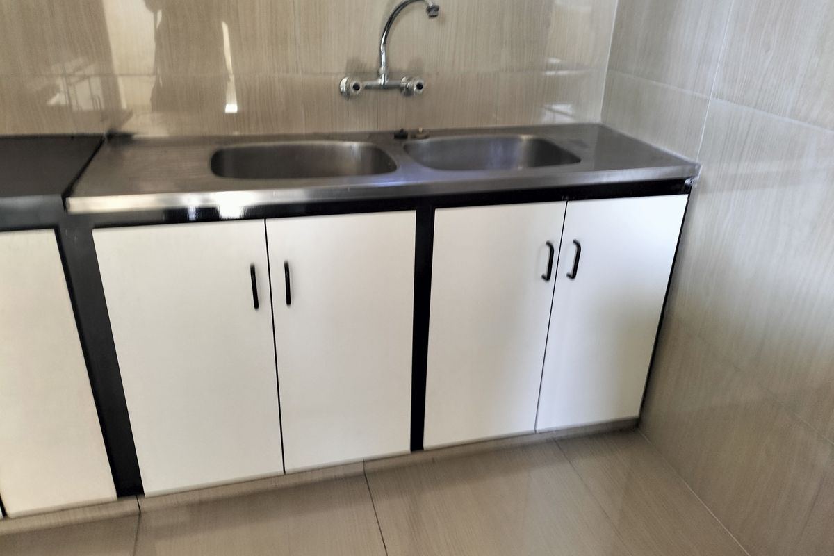 A functional kitchen area featuring a stainless steel double sink, chrome faucet, and white base cabinetry with tiled backsplash and flooring.