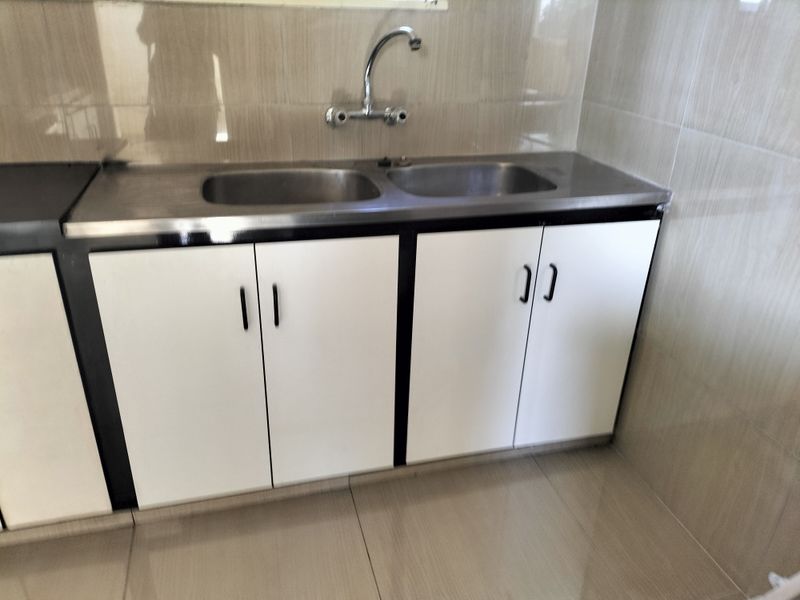A functional kitchen area featuring a stainless steel double sink, chrome faucet, and white base cabinetry with tiled backsplash and flooring.