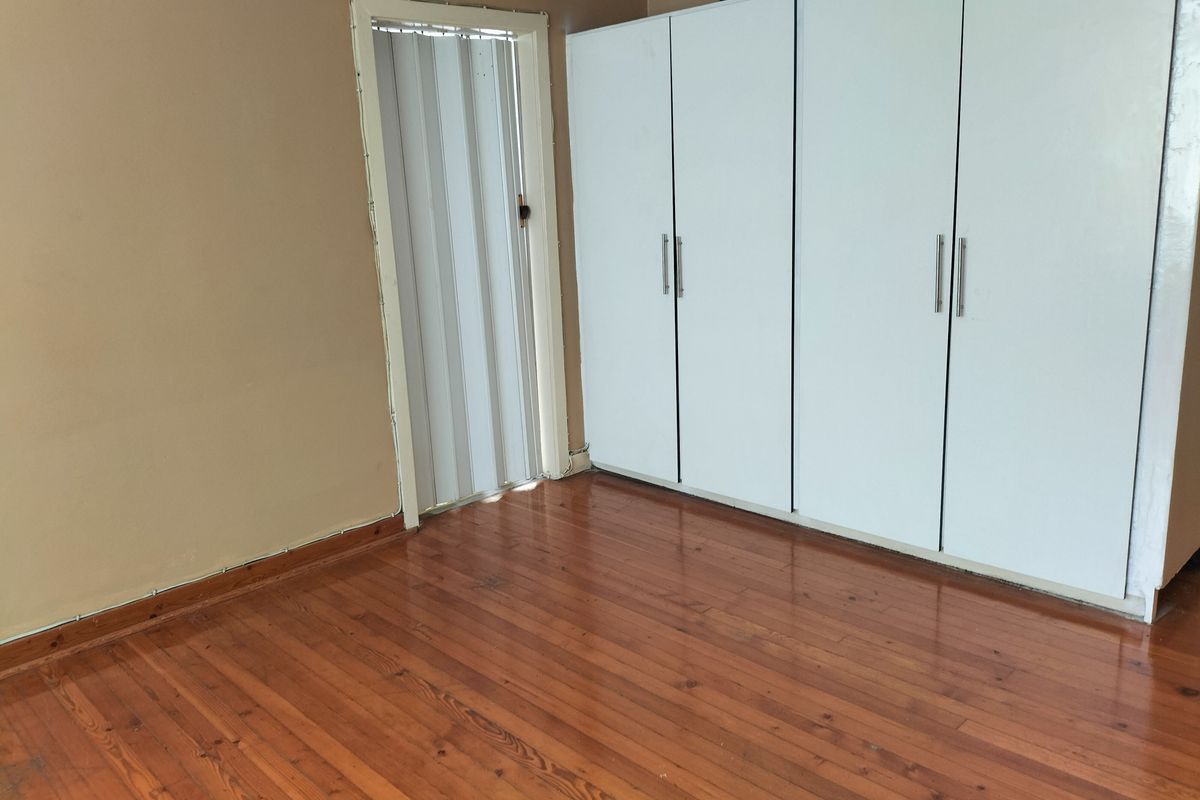 A bedroom featuring polished timber flooring, built-in white cupboards, and a folding door, presenting a clean, vacant space ready for personalization.